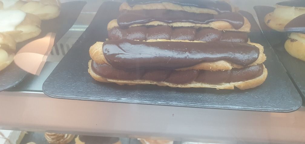 Éclairs de chocolate en una bandeja de servir negra en la vitrina de una panadería.