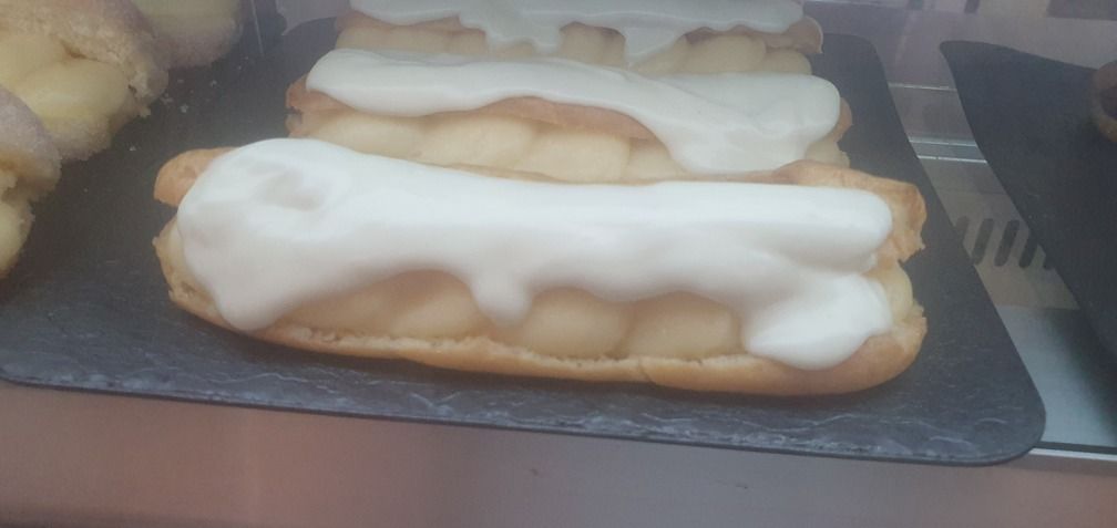 Éclairs con glaseado blanco en una bandeja negra. Productos horneados en una pastelería.