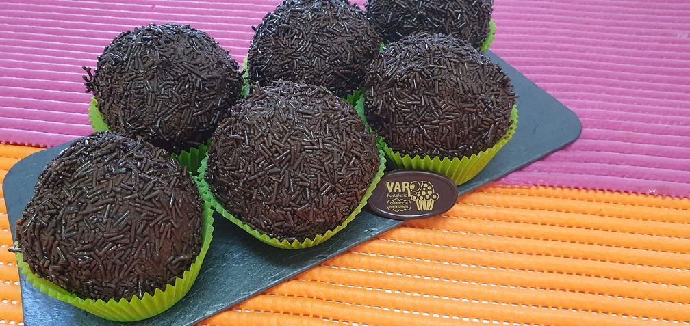 Brigadeiros de chocolate en capacillos verdes sobre un plato gris oscuro.
