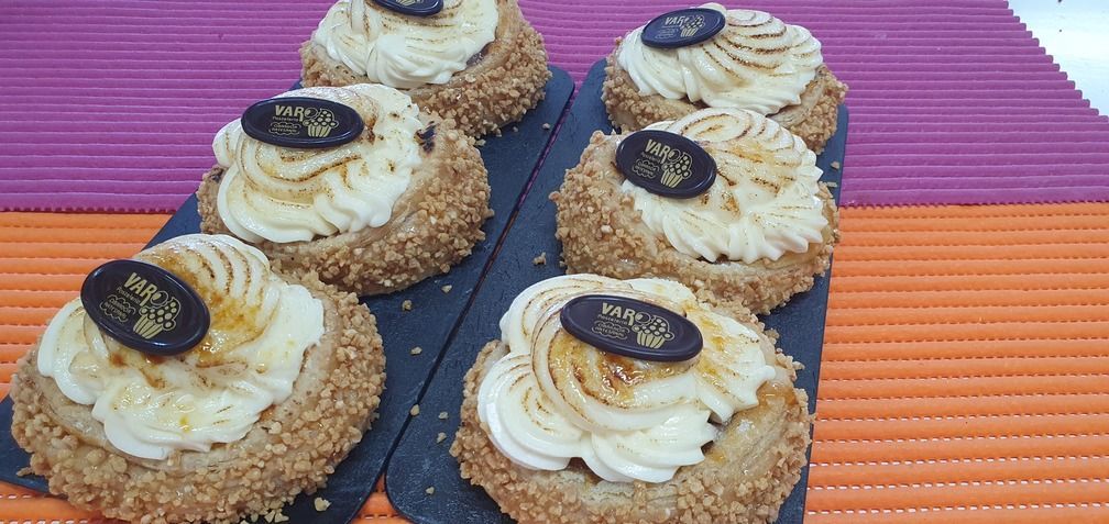 Seis pasteles rellenos de crema con corteza de nueces, cubiertos con medallones de chocolate, dispuestos sobre una tabla negra.