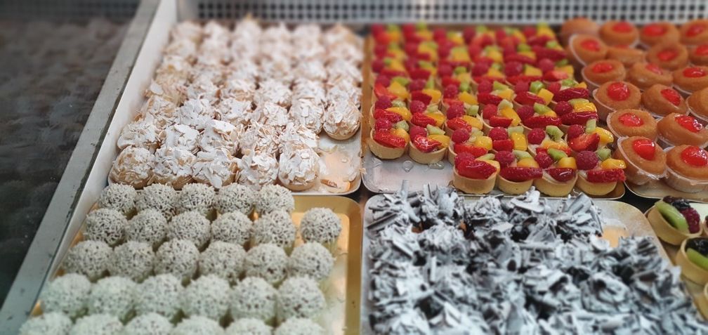 Vitrina repleta de pasteles variados: bolas de coco, tartaletas de frutas y virutas de chocolate.