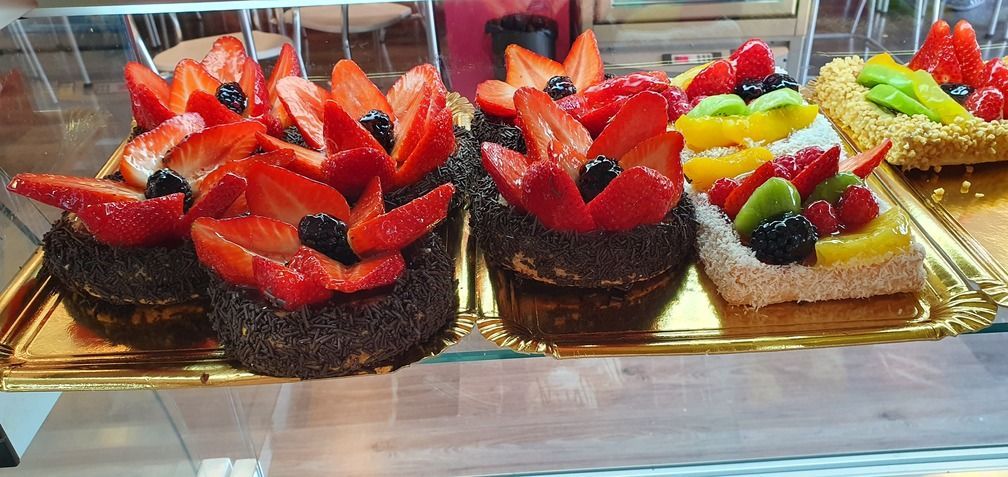 Varias tartas de frutas con coberturas coloridas exhibidas en una bandeja dorada, presumiblemente en una panadería.