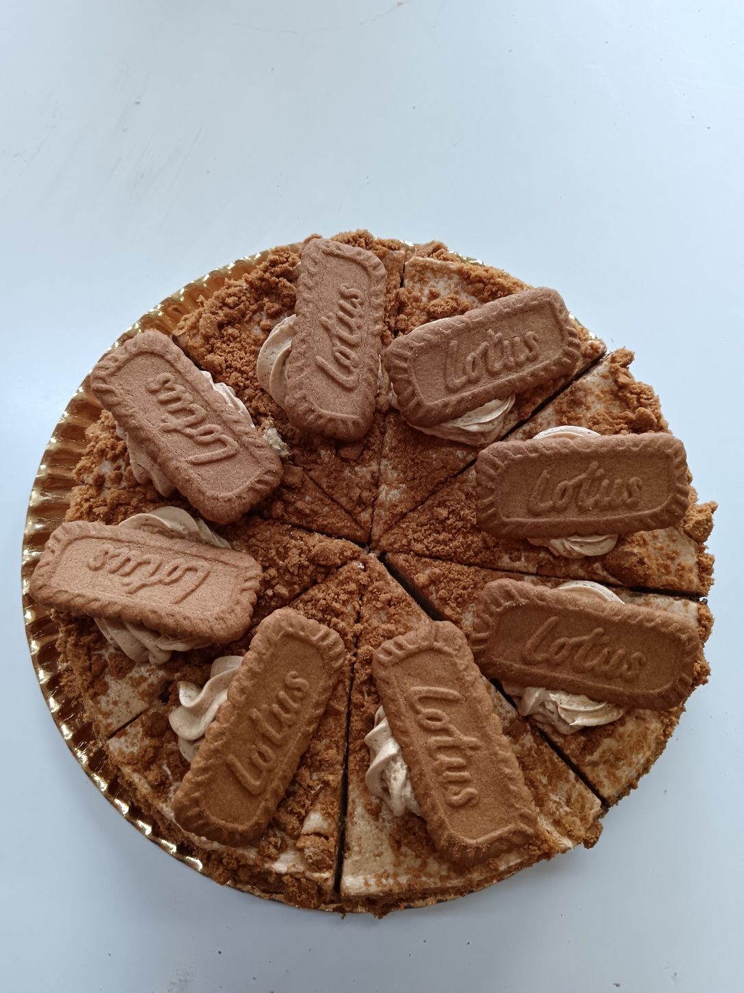 Pastel de galleta Lotus, redondo, cortado en rodajas, cubierto con crema y galletas, sobre una superficie de color azul claro.