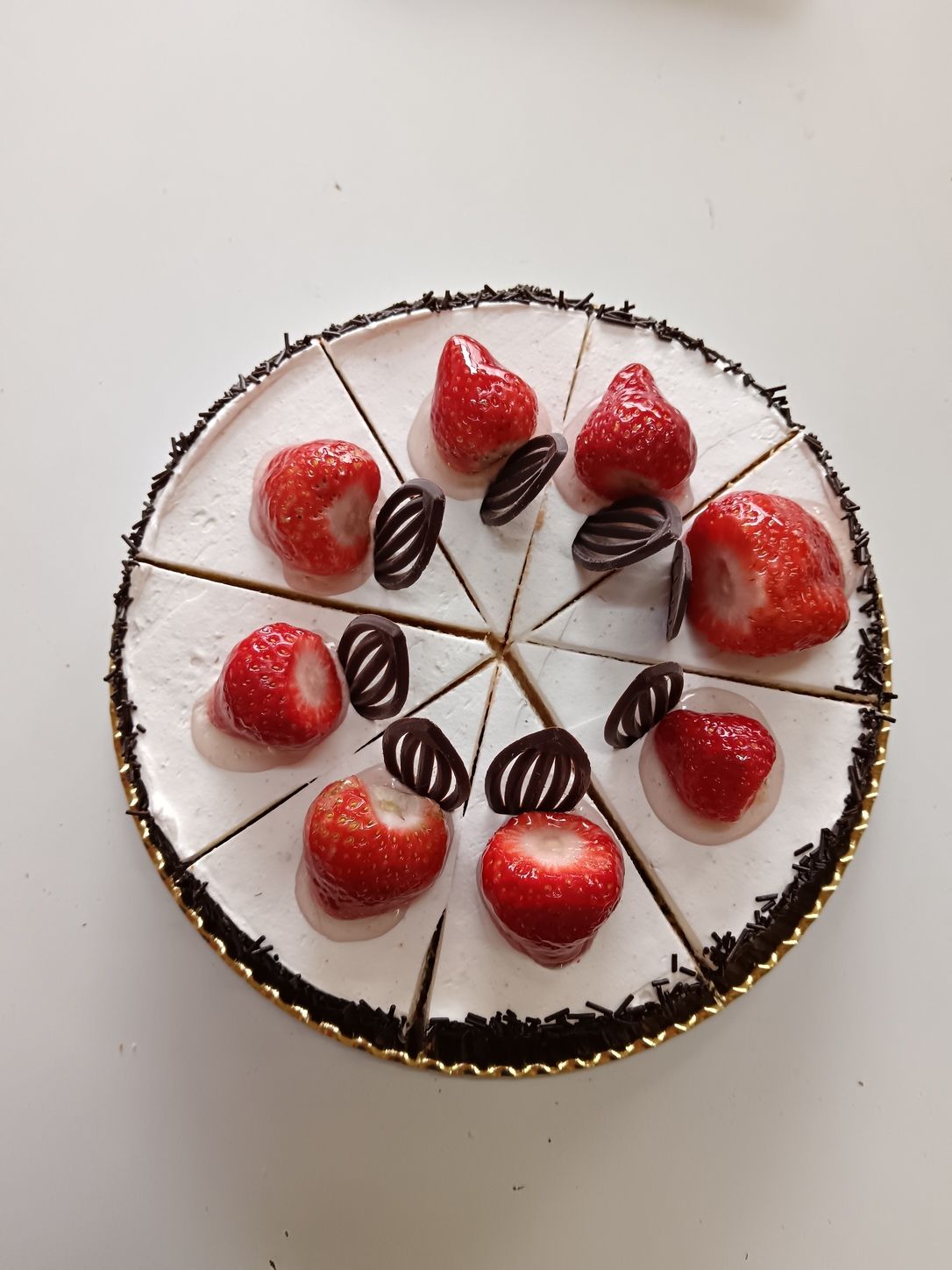 Pastel de fresas con glaseado blanco, cortado en rodajas, decorado con rizos de chocolate y fresas enteras.