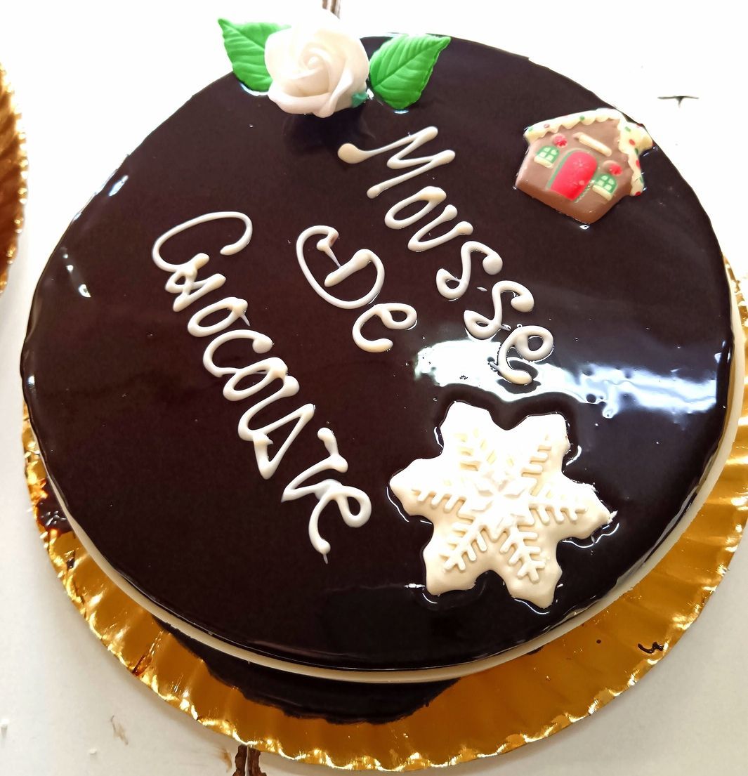 Pastel de mousse de chocolate con letras de glaseado blanco, copos de nieve y decoraciones de casas de jengibre.