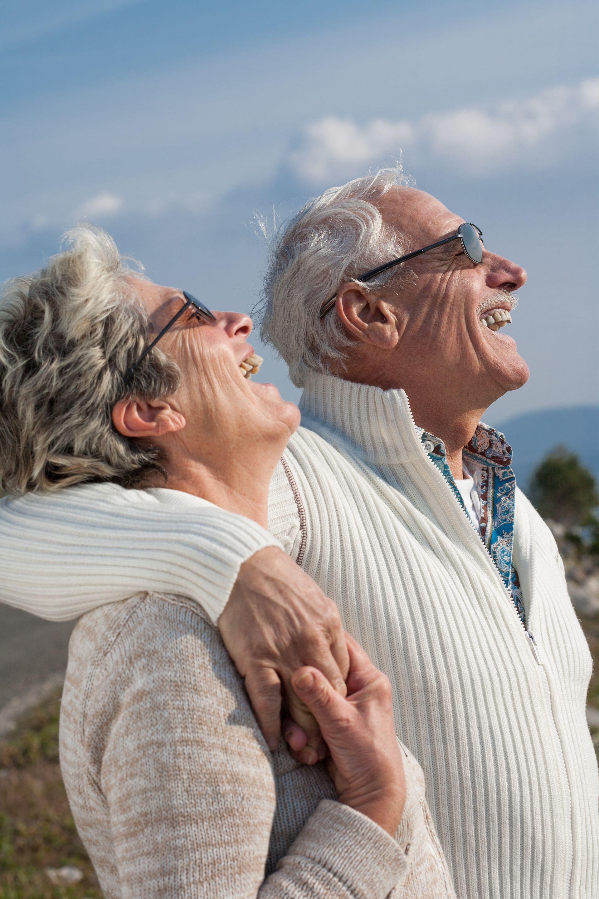 Un couple âgé, enlacé, rit en regardant vers le ciel.