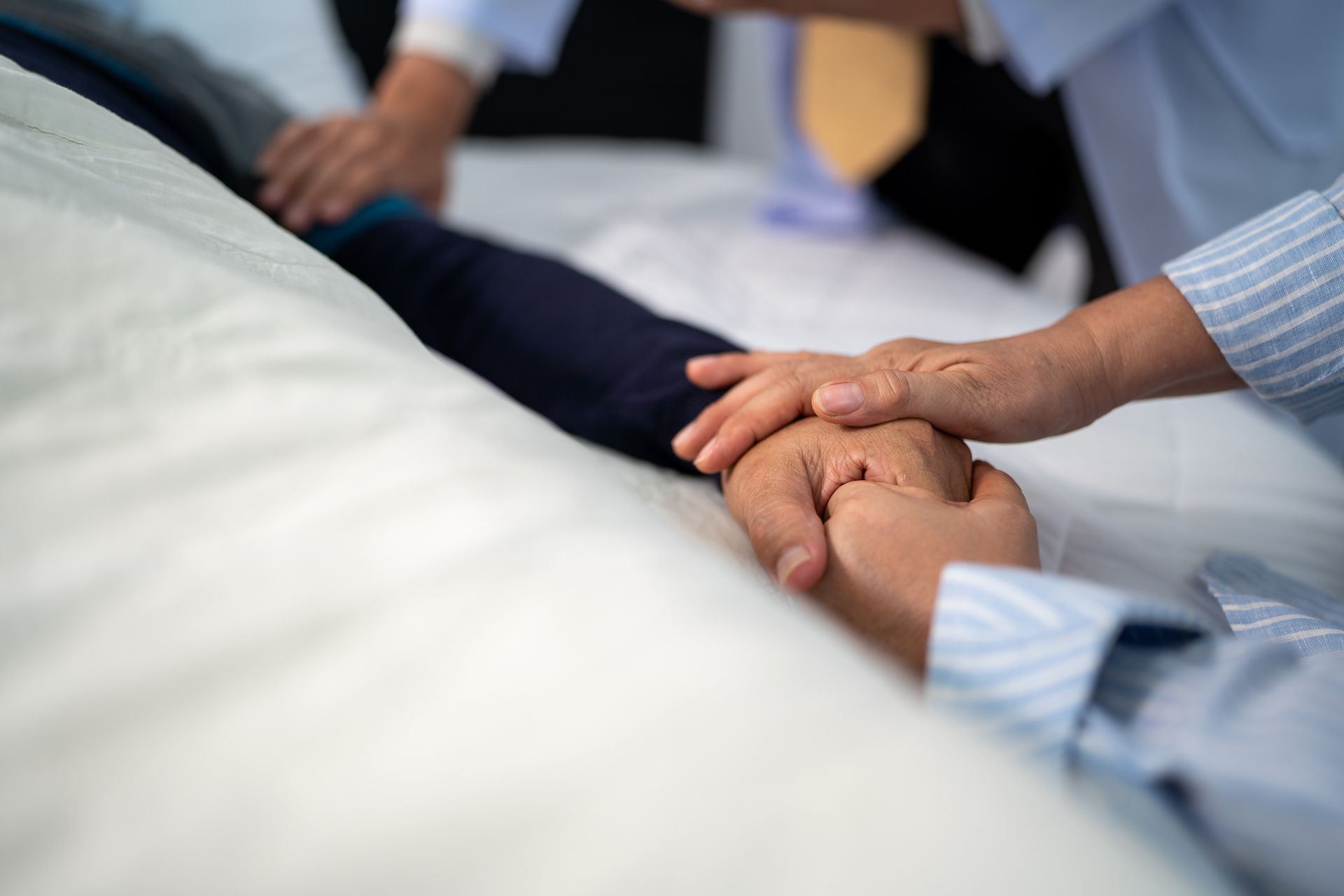 Une personne qui tient la main de quelqu'un allongé dans un lit.
