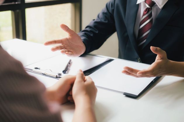 Un homme en costume fait des gestes tout en discutant d'un contrat avec une autre personne.