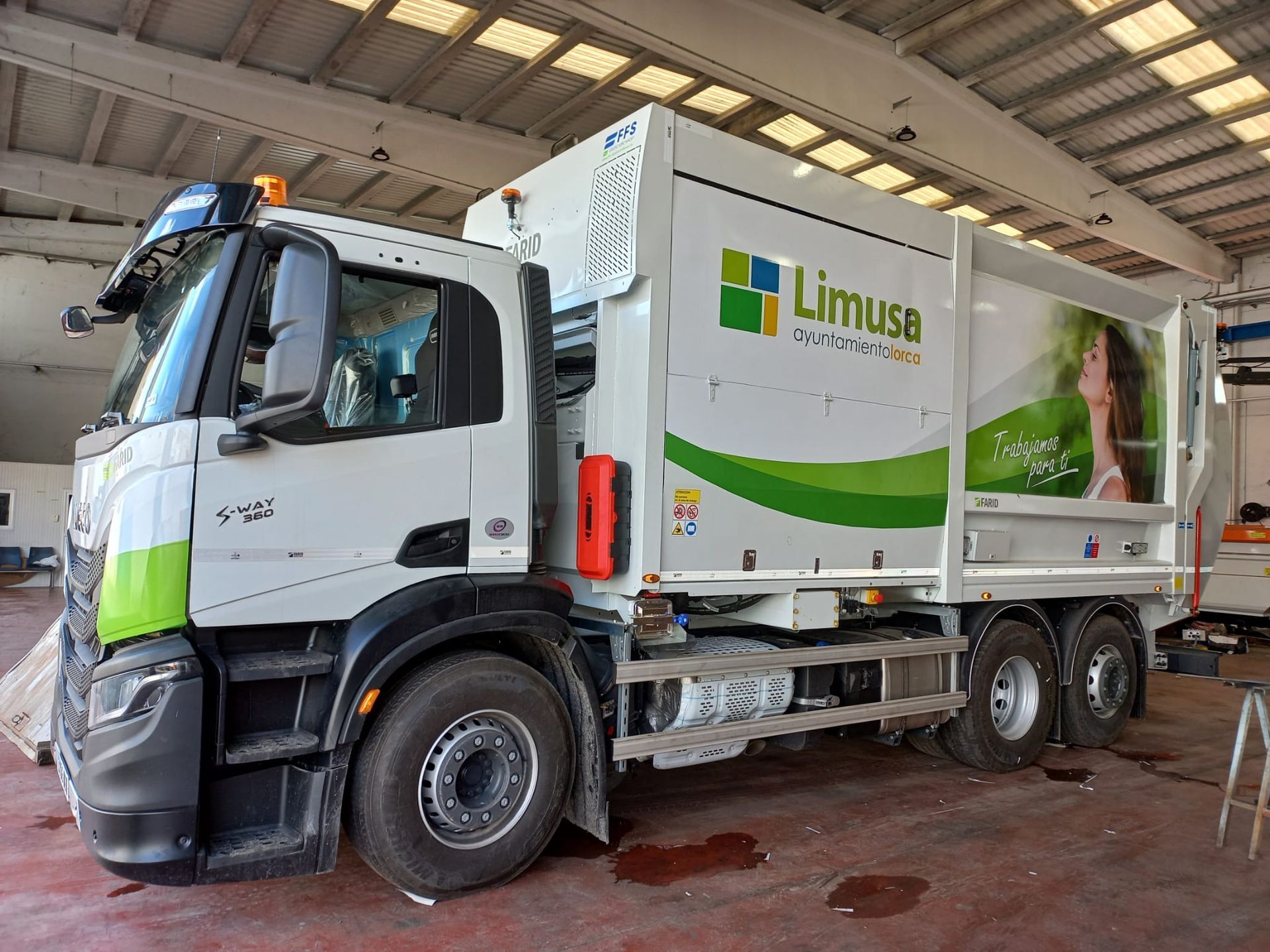 Un camión de basura blanco y verde está estacionado en un garaje.