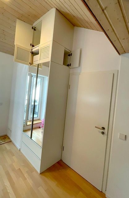 ein weißer Kleiderschrank mit einem Spiegel und einer Tür in einem Zimmer.