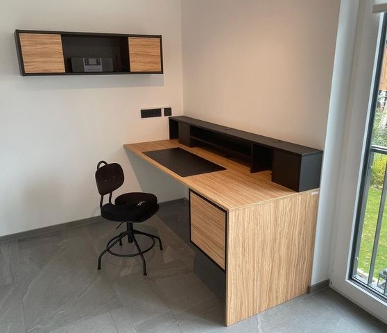 Ein Holzschreibtisch mit einem schwarzen Stuhl in einem Zimmer