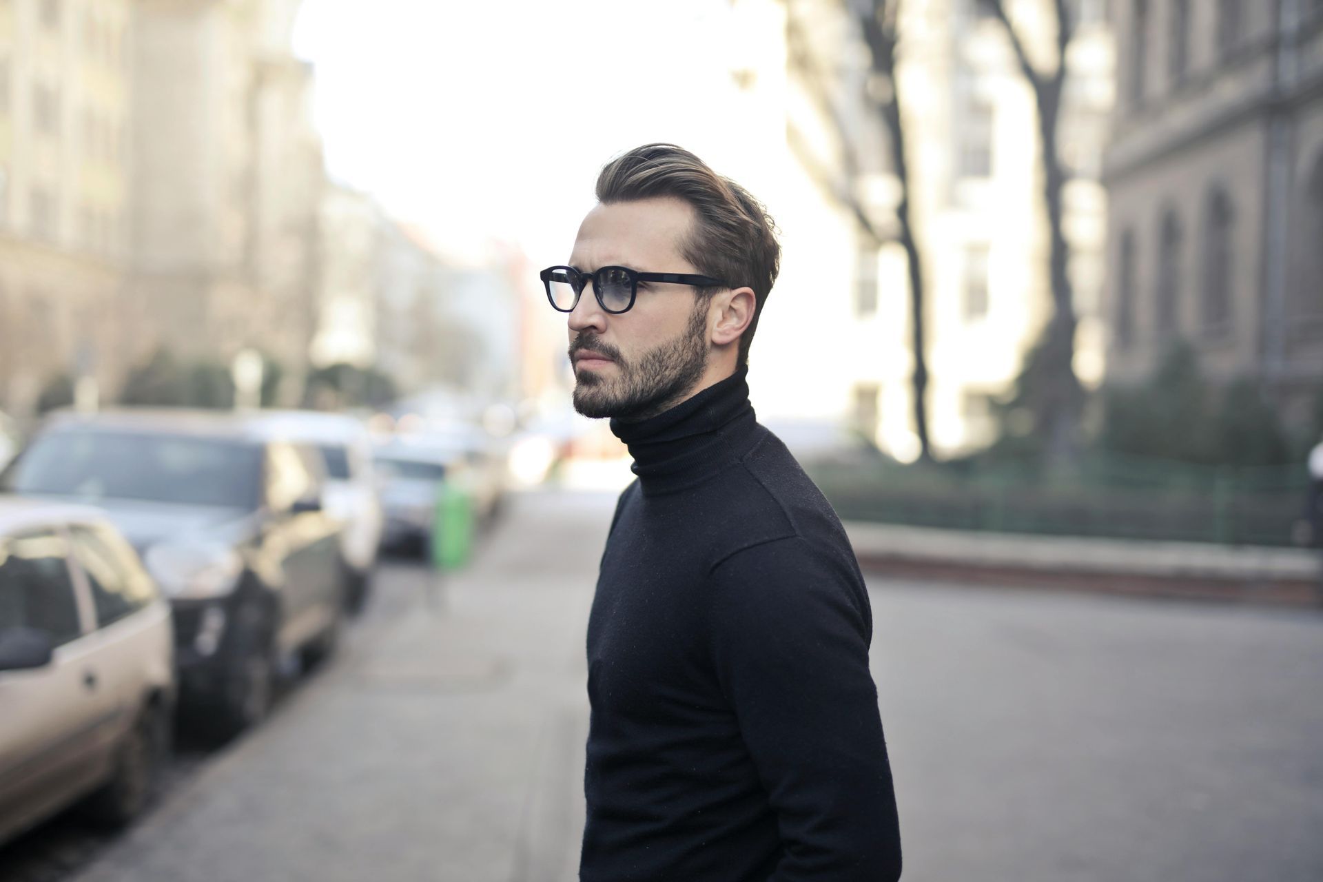 Un uomo che indossa occhiali e un dolcevita nero sta camminando lungo una strada.