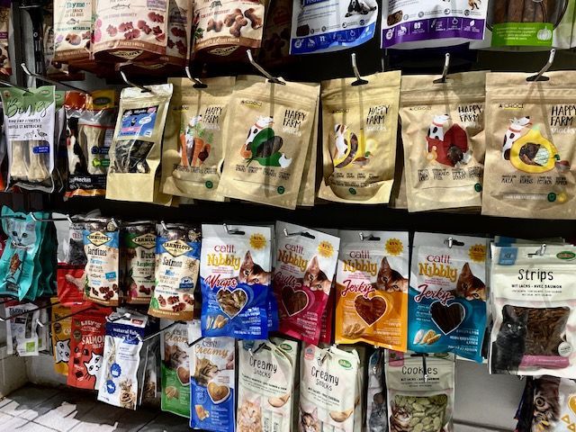 Des étagères remplies de friandises pour animaux de compagnie emballées, de couleurs et de motifs variés, dans un magasin.