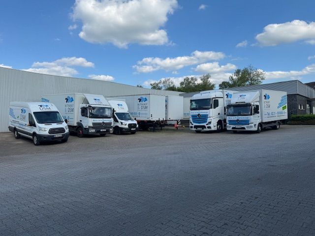 Mehrere weiße Lieferwagen parkten vor einem Lagerhaus unter bewölktem Himmel.