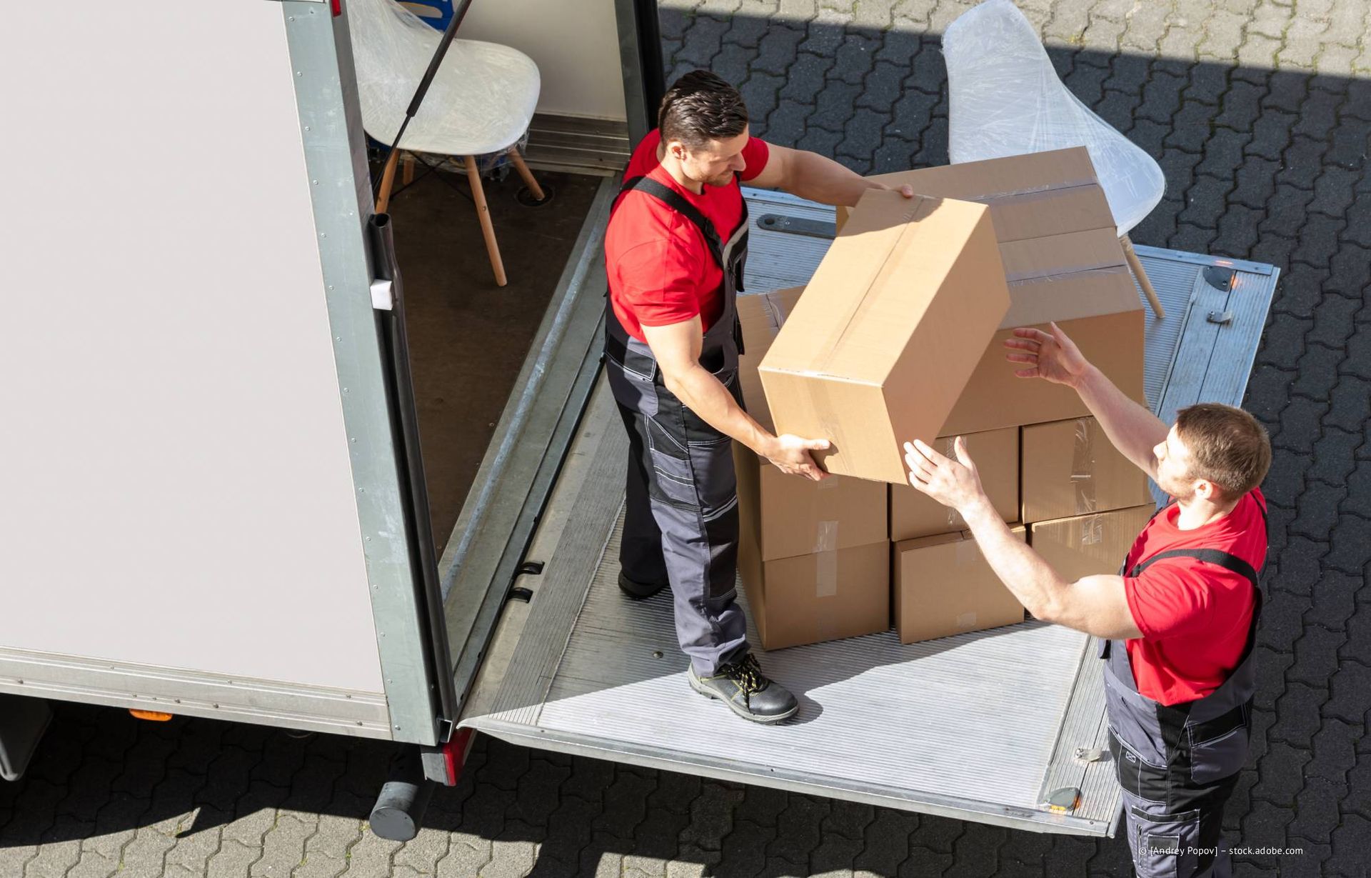 Zwei Umzugshelfer in roten Hemden laden Kartons in einen Lastwagen.