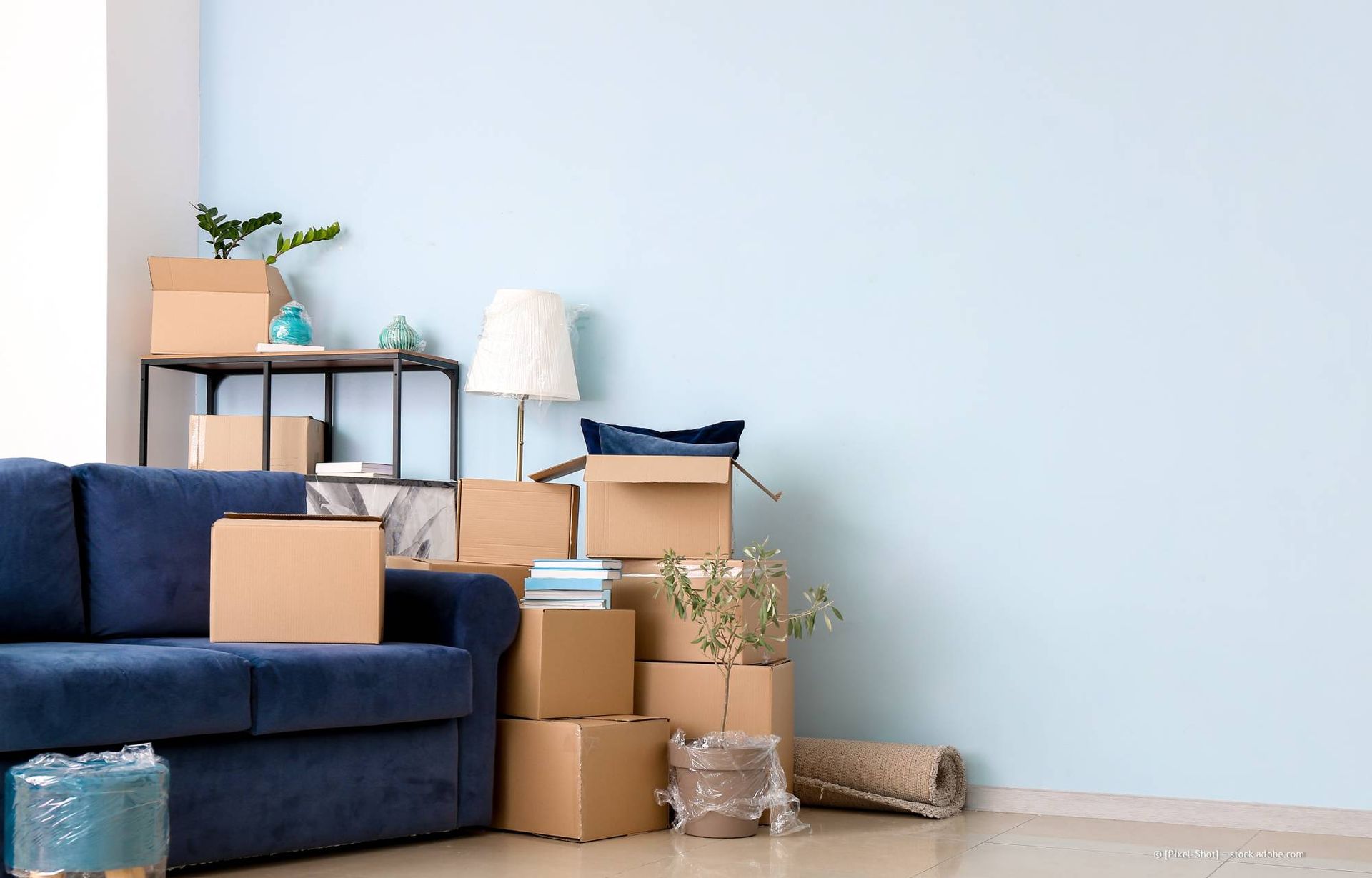 Zimmer mit Umzugskartons, blauem Sofa, Tisch und hellblauer Wand.