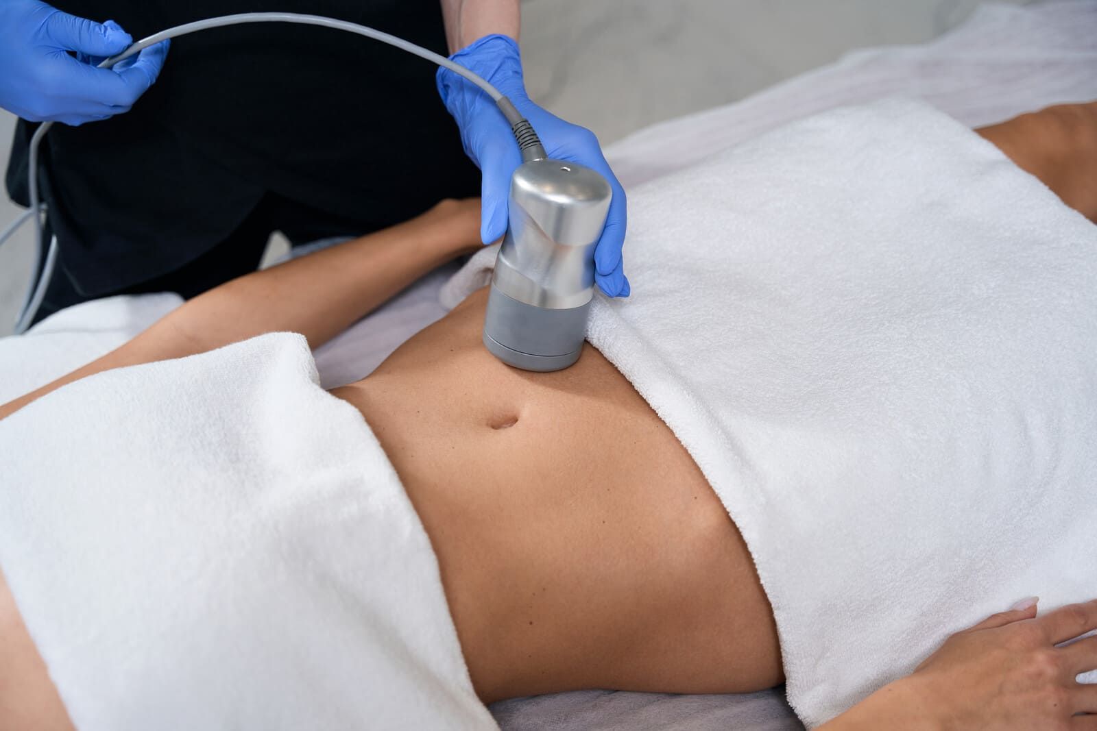 Persona recibiendo tratamiento corporal en una camilla de masaje. Se utiliza un dispositivo manual sobre el abdomen.