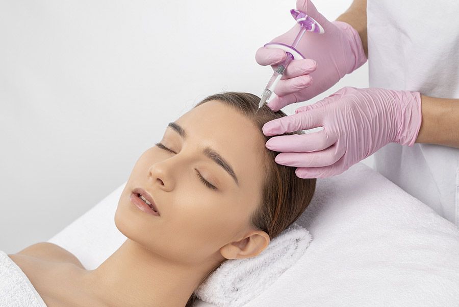 Persona que recibe una inyección en el cuero cabelludo con manos enguantadas, en un entorno médico.