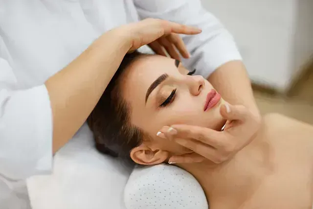 Masaje facial en un spa, donde las manos acarician suavemente el rostro de un cliente relajado.