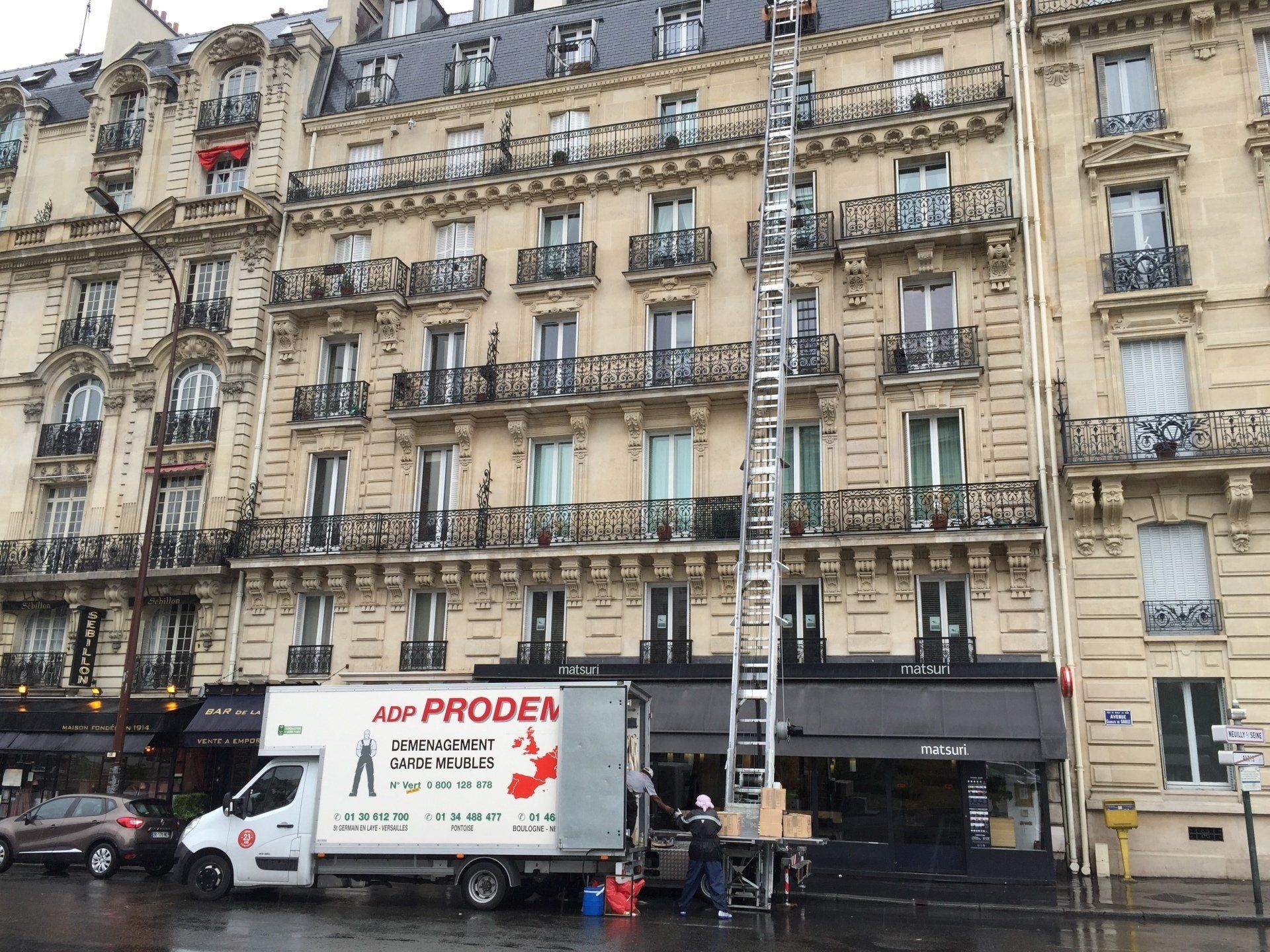 Camion de déménagement garé dans une rue devant un immeubel de plusieurs étages ainsi qu'une échelle