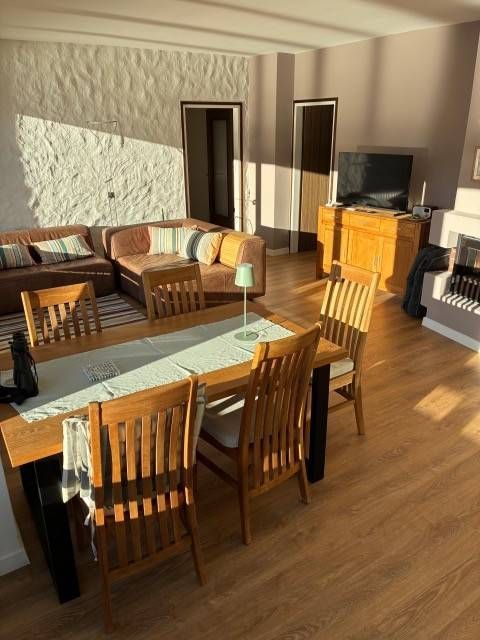 Wohnzimmer mit Esstisch, Ecksofa, Kamin und Holzboden, lichtdurchflutet.