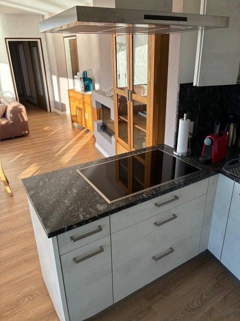 Balkon mit Blick auf einen See mit einer Insel. Ausgestattet mit Tisch, Stühlen und einem geschlossenen Sonnenschirm. Berge in der Ferne.