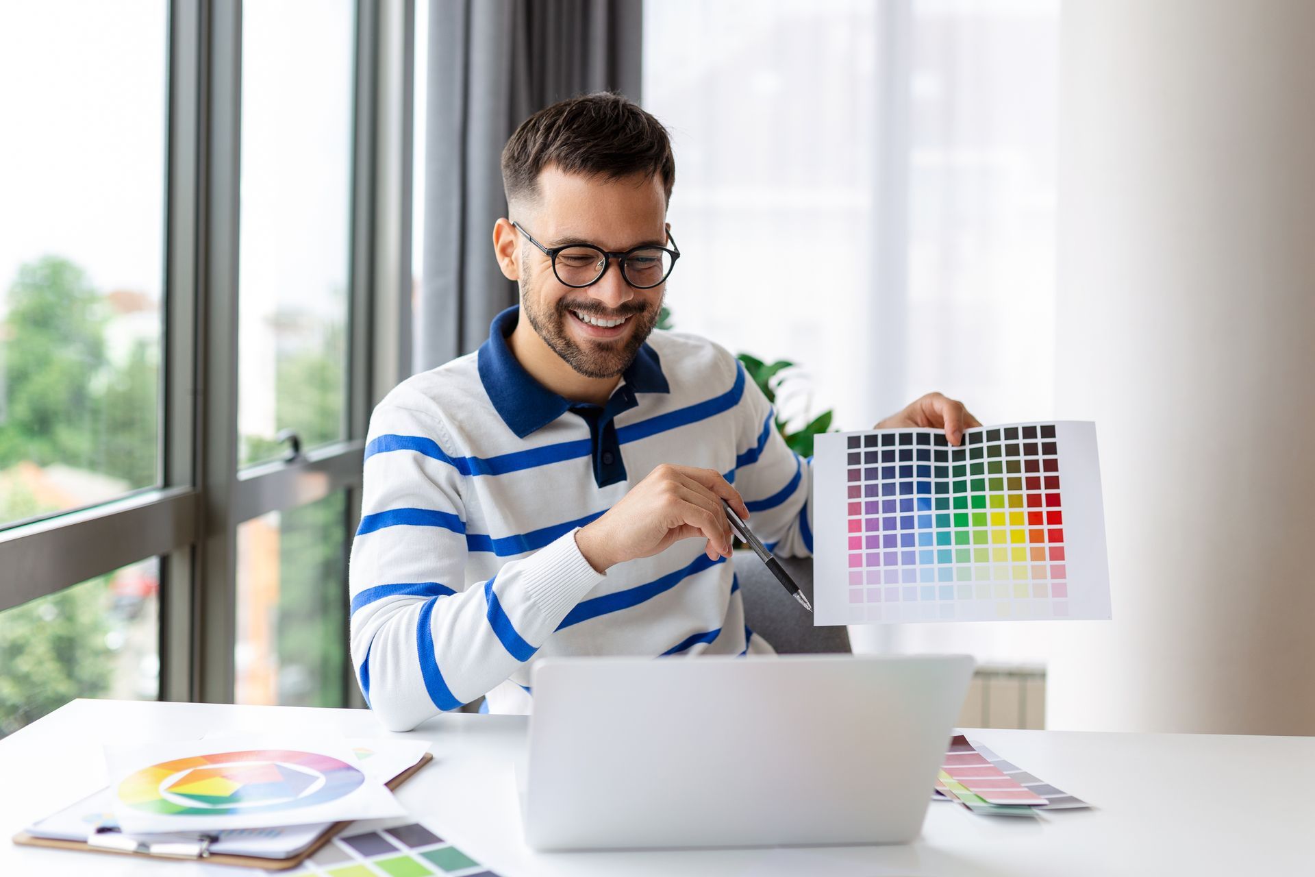 Homme souriant présentant un nuancier de couleurs vers son écran d'ordinateur