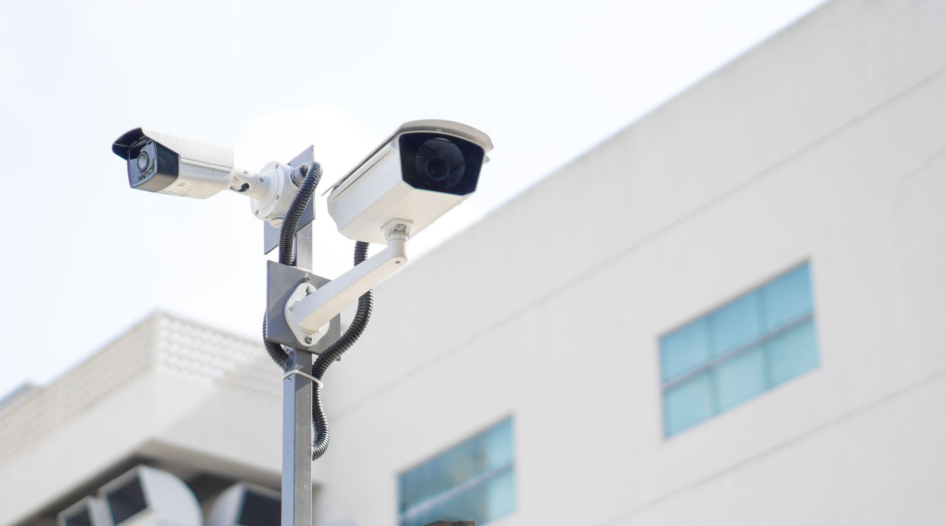 Deux caméras de sécurité blanches fixées sur un poteau à l'extérieur d'un bâtiment moderne