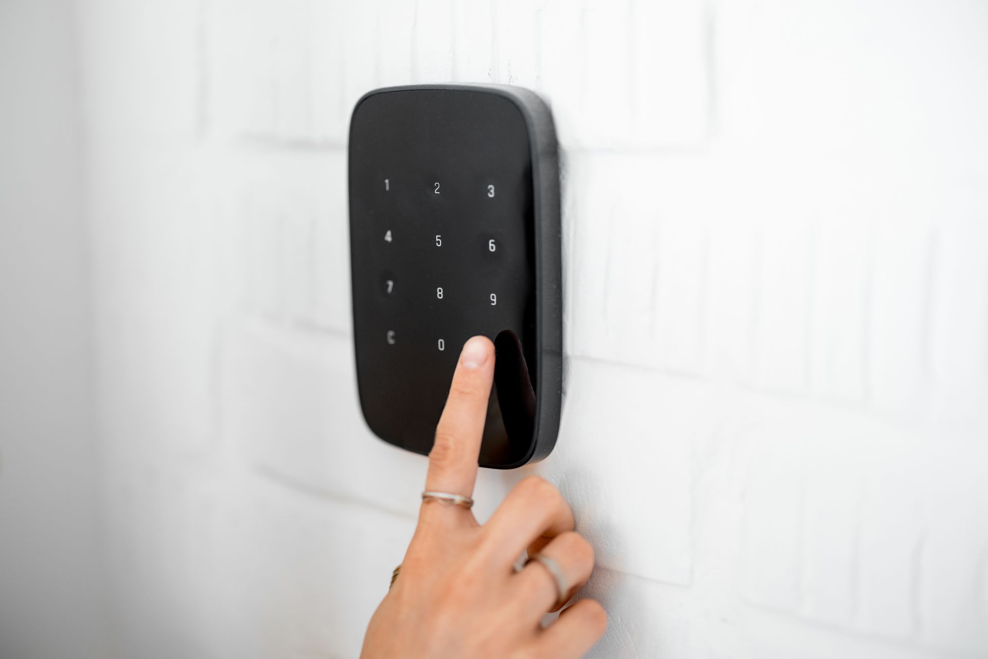 Main saisissant un code sur une serrure à clavier murale noire.