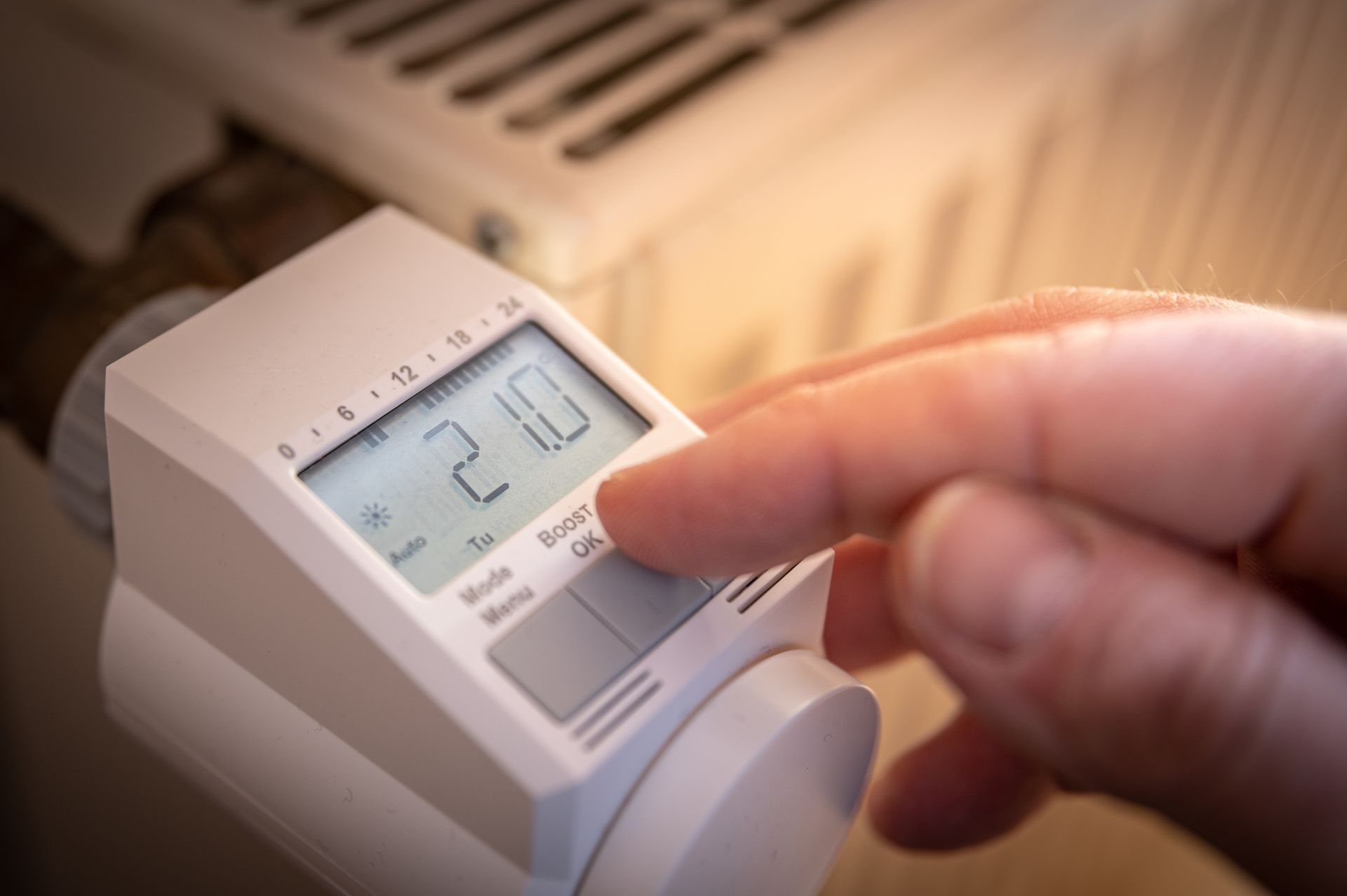 Doigt ajustant un thermostat blanc indiquant 21,0°C à l'intérieur