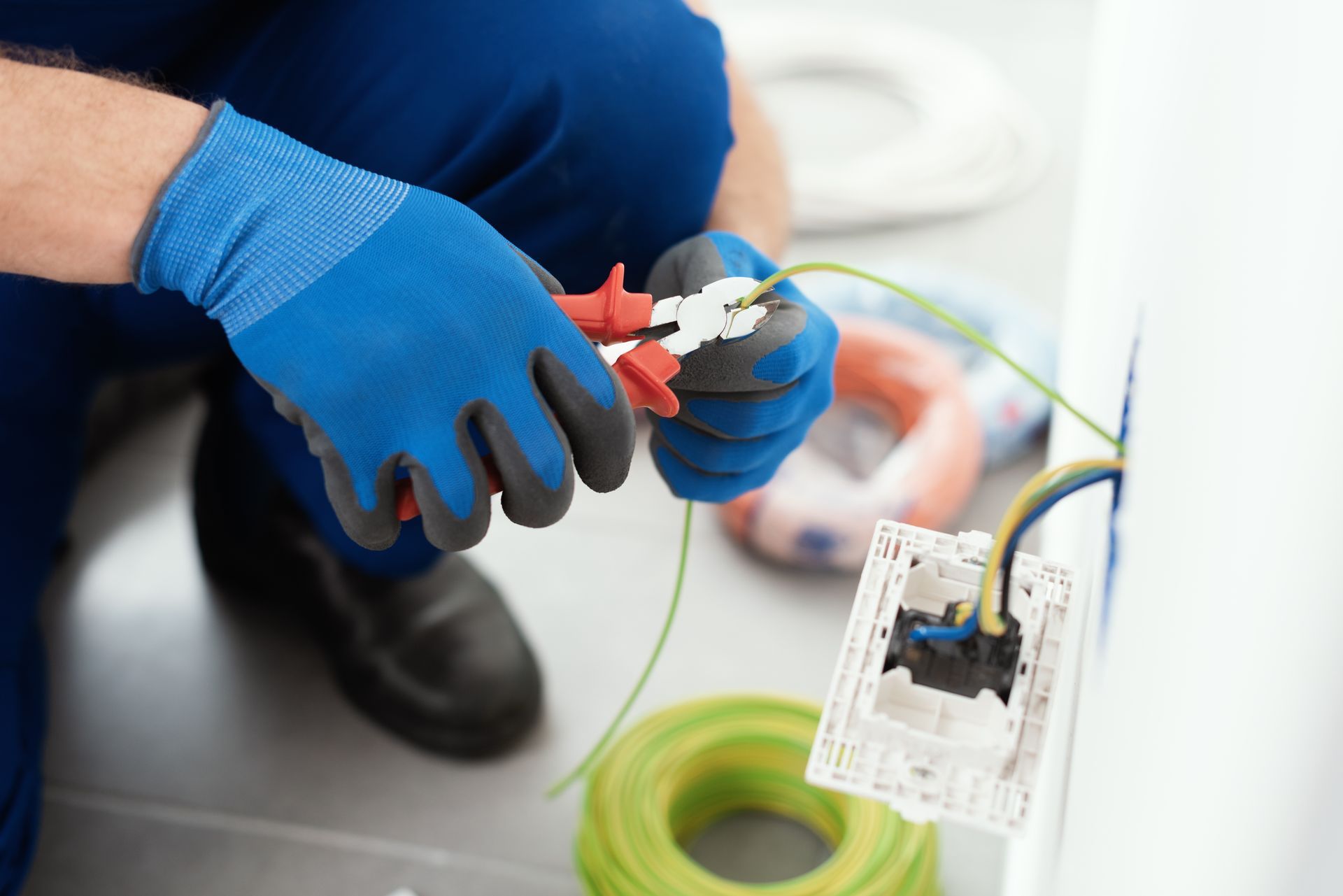 Un technicien portant des gants bleus sertit un câble près d'une prise électrique ; outils et câbles sont visibles.