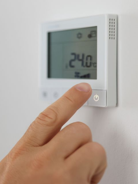 Doigt appuyant sur un thermostat numérique blanc affichant 24,0° sur un mur