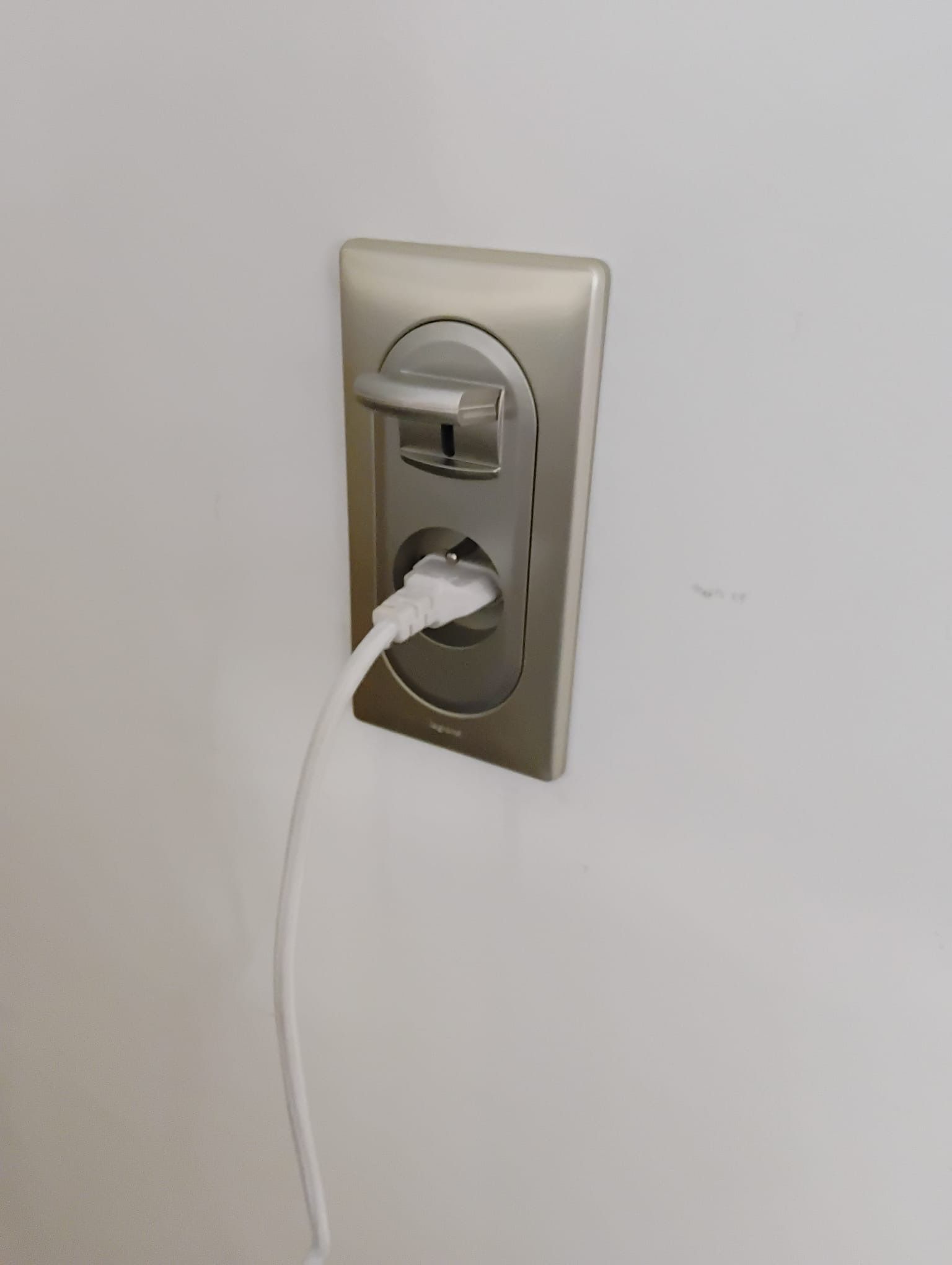 Prise murale avec un câble de chargement blanc branché dans la prise inférieure sur une plaque beige.