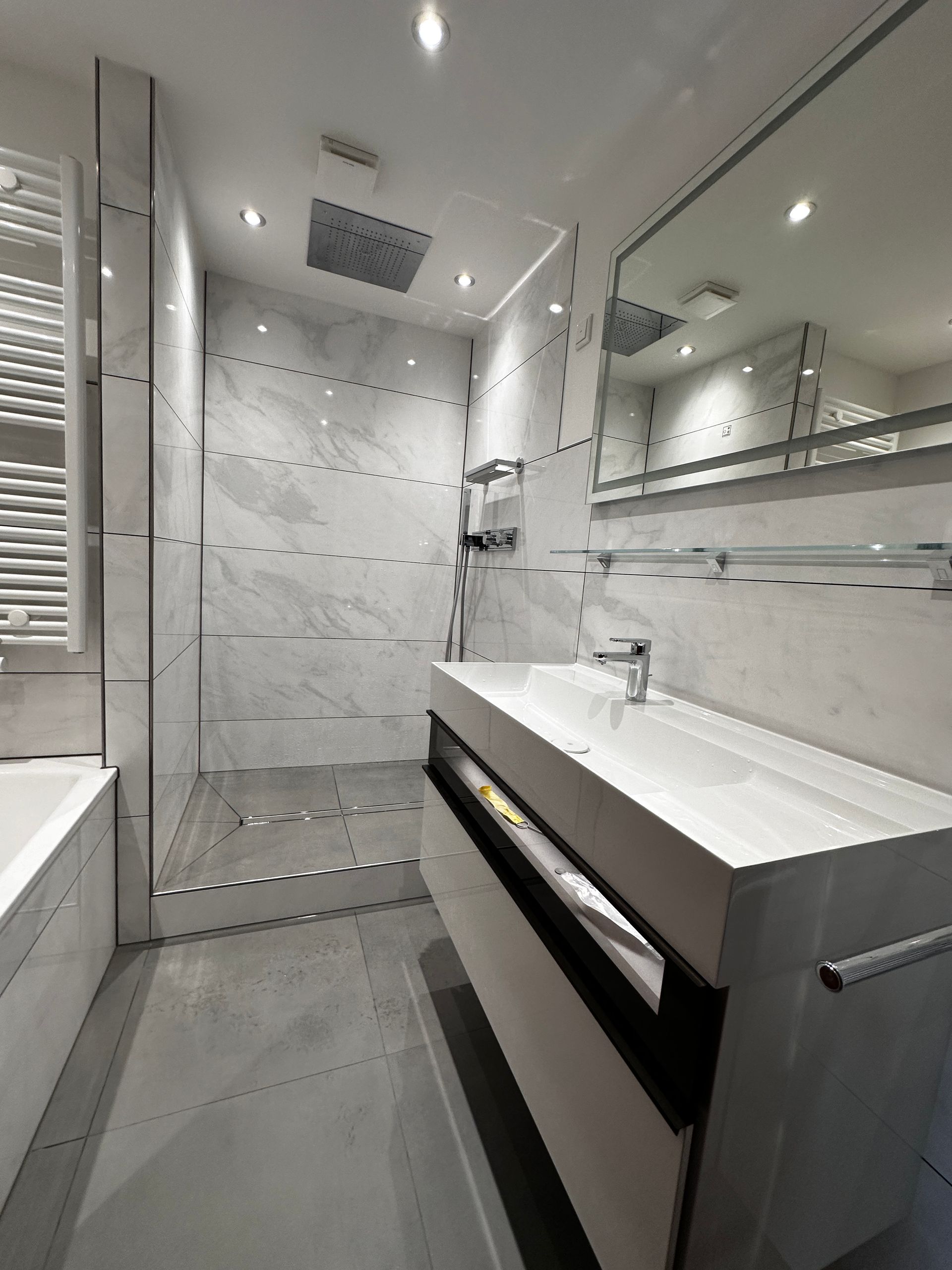 Ein Badezimmer mit Waschbecken, Spiegel und ebenerdiger Dusche