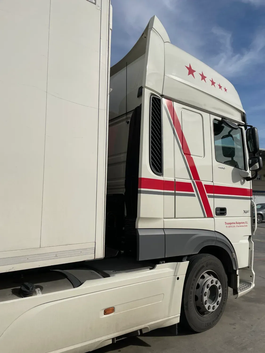 Un camión blanco con rayas rojas en el costado está estacionado en un estacionamiento.