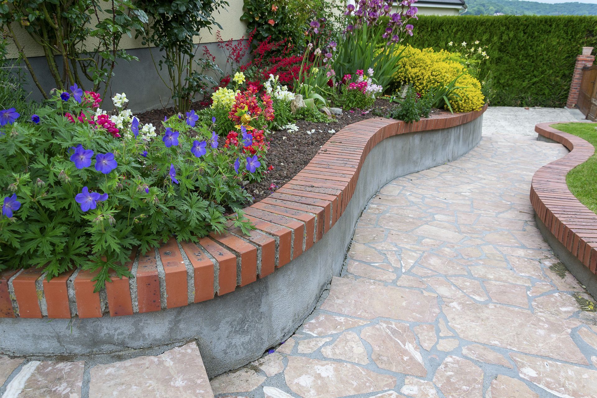 Parterre de fleurs bordé de briques, orné de fleurs et d'un chemin de pierres sinueux.