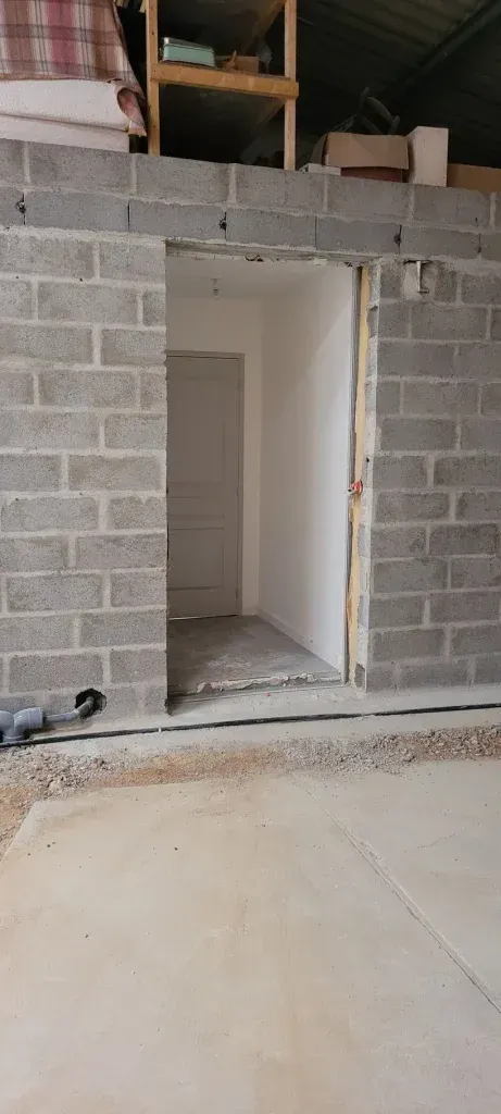 Vue intérieure d'une porte dans un bâtiment en construction, aux murs en parpaings gris.
