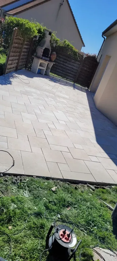 Terrasse avec dalles de pierre, barbecue et pelouse entretenue par un robot tondeuse.