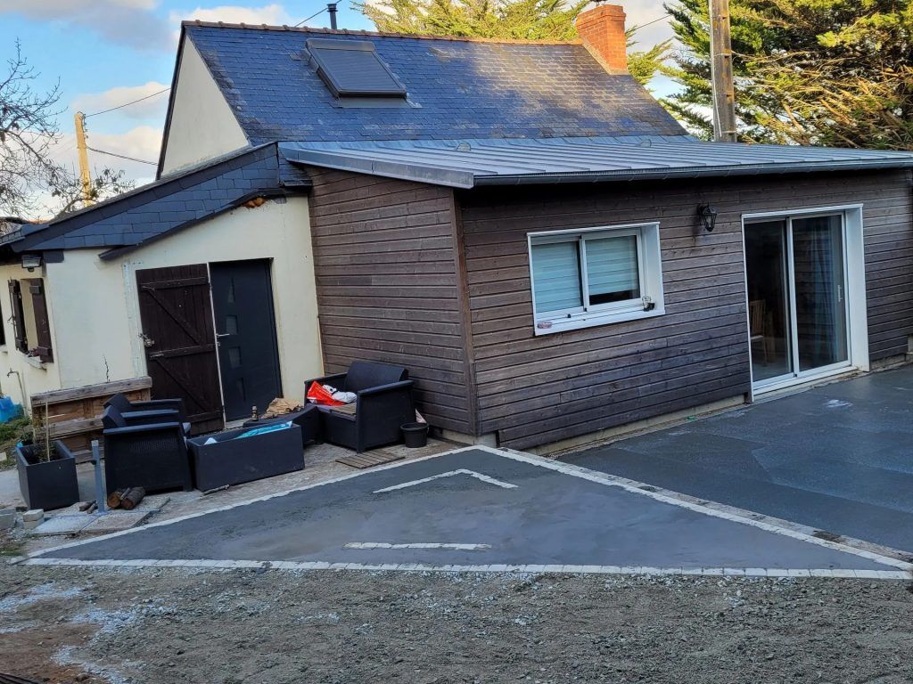 Maisonnette avec une dépendance aux murs bruns avec une porte coulissante et une terrasse bétonnée.