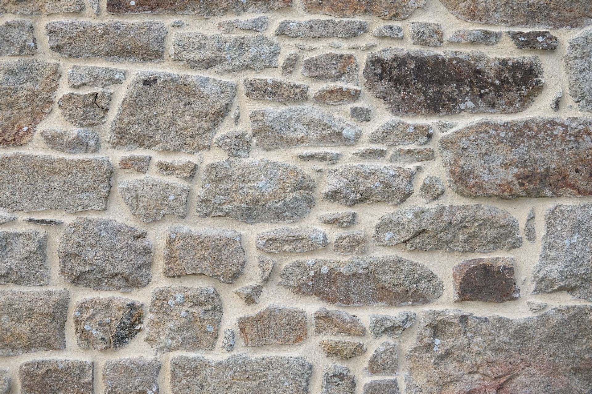 Mur en pierre avec des pierres grises et brunes, mortier clair.