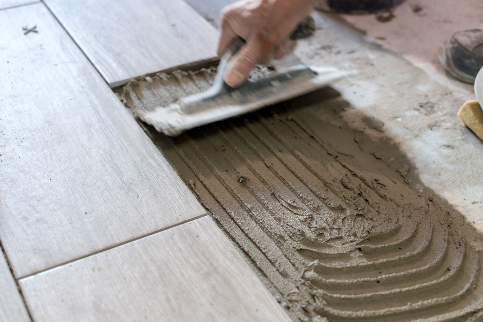 Vers page revêtements de sols Personne utilisant une truelle crantée pour étaler le mortier pour poser du carrelage.