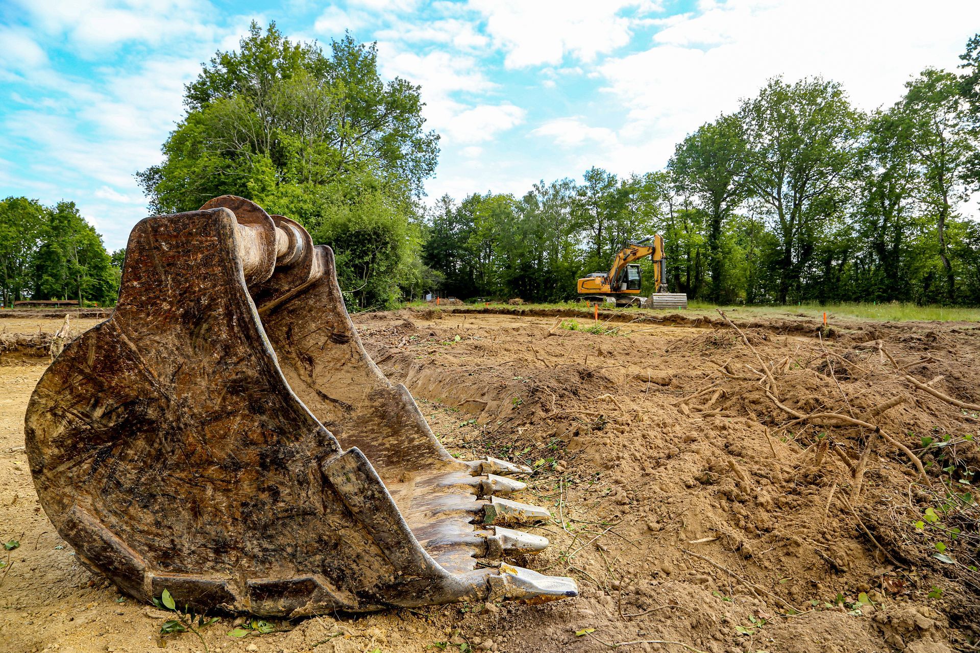 Vers page terrassement Au premier plan, un godet d'excavatrice ; à l'arrière-plan, une excavatrice jaune.