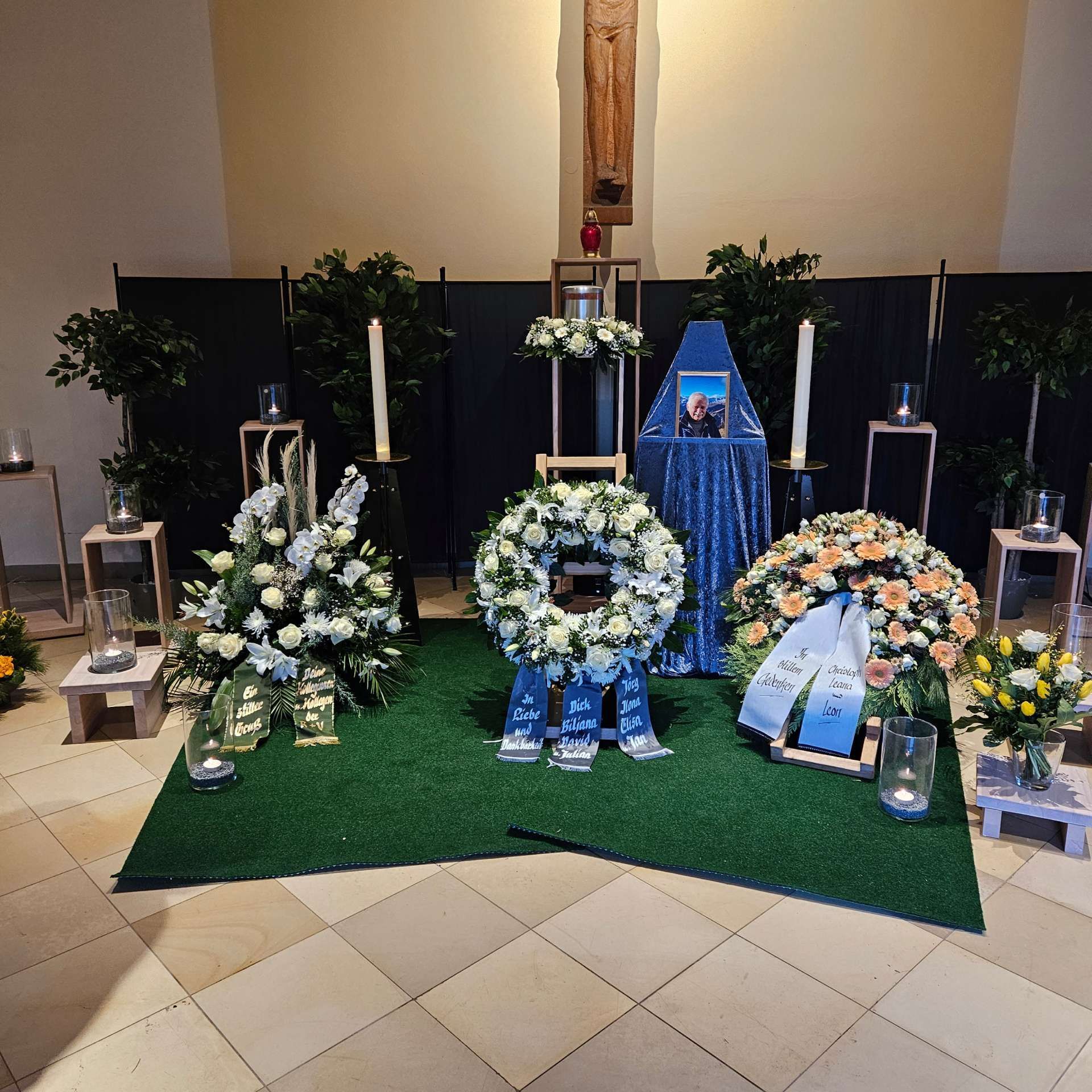 Trauerdekoration mit Blumenarrangements und einem Gedenkfoto in einer Kapelle.
