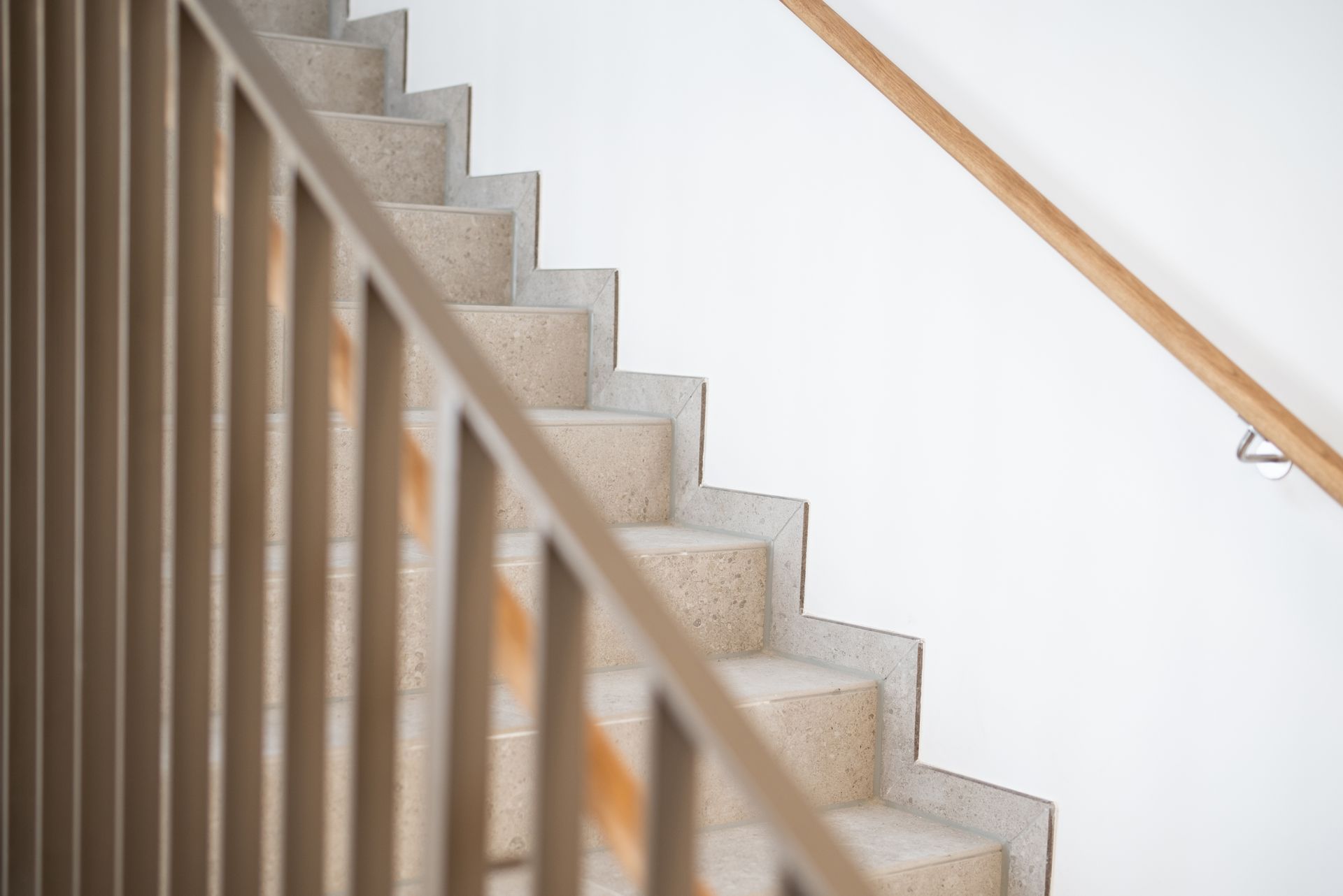 Treppe mit Metallgeländer auf einer Seite und Holzhandlauf an weißer Wand.