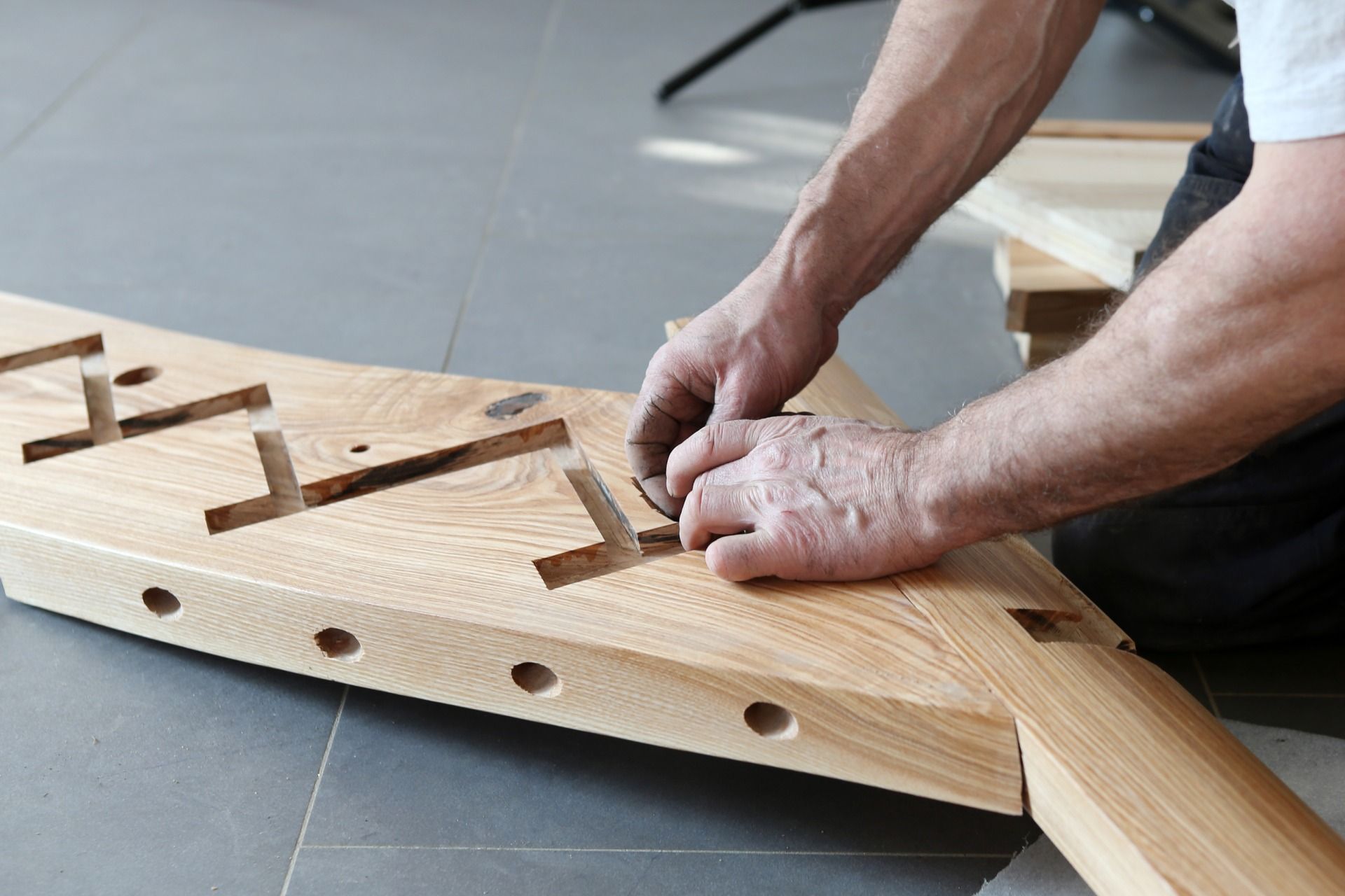 Eine Person montiert eine Holztreppe mithilfe von Werkzeugen auf einem hellen Holzbrett.