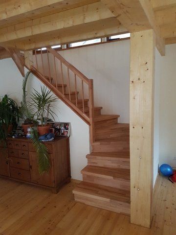 Holztreppe in einem Haus mit Holzböden, Geländer und Stützbalken, mit einem Seitenschrank.