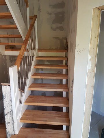 Holztreppe mit weißem Geländer, unfertigen Wänden und einer Türöffnung.