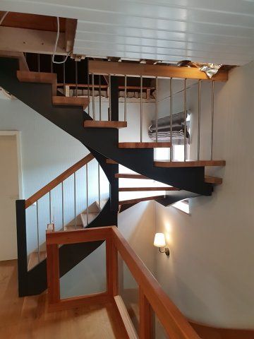 Treppe mit Holzstufen, schwarzem Rahmen, Metallgeländer und einem Holzhandlauf in einem Haus.