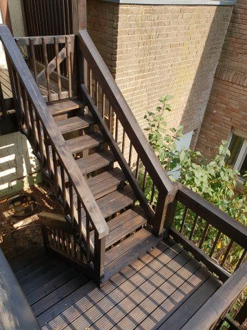 Eine hölzerne Außentreppe an einem Backsteingebäude führt nach unten.
