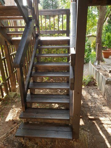 Nach oben führende Holztreppe im Freien, dunkelbraunes Geländer, Licht, das durch die Bäume im Hintergrund fällt.